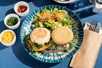 A bun of scrambled eggs and white cottage cheese served with vegetables and greens on a beautifully decorated plate, a breakfast set, illuminated by the morning sun.