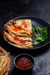 Pancakes with red caviar in a black plate close-up on the table. Breakfast Maslenitsa