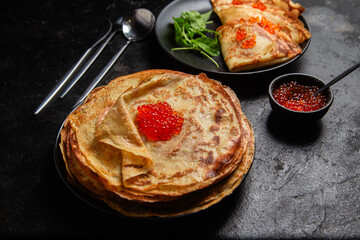 Pancakes with red caviar in a black plate close-up on the table. Breakfast Maslenitsa