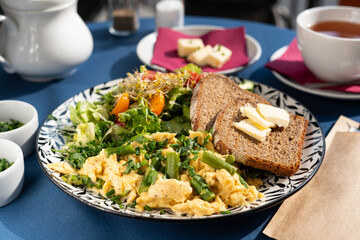 Scrambled eggs with vegetables, asparagus, toast, chives, seed sprouts and greens served on a beautifully decorated plate, a breakfast set, illuminated by the morning sun.