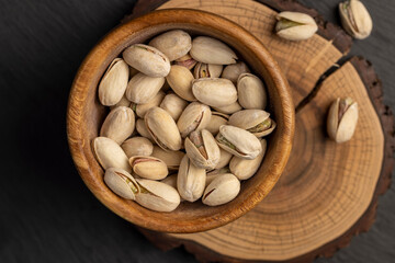 pistachio in shells with added salt, unpeeled pistachio nuts in a wooden bowl with cracked shells