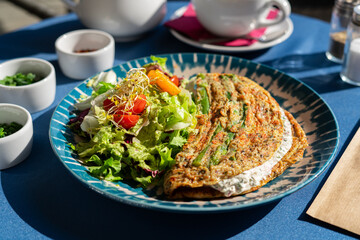 Omelette with cottage cheese and fresh vegetables served on a beautiful blue and white plate. A breakfast set illuminated by the morning sun.