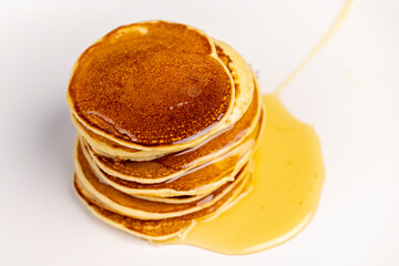 pancakes stacked together on a white bowl, a tower of small milk pancakes on a ceramic bowl with bee honey