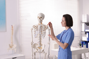 Doctor pointing at parts of human skeleton model in clinic