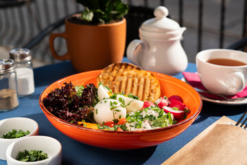 Hard-boiled eggs and white cottage cheese served with vegetables, toast, cherry tomatoes and greens on a beautifull orange plate, a breakfast set, illuminated by the morning sun.