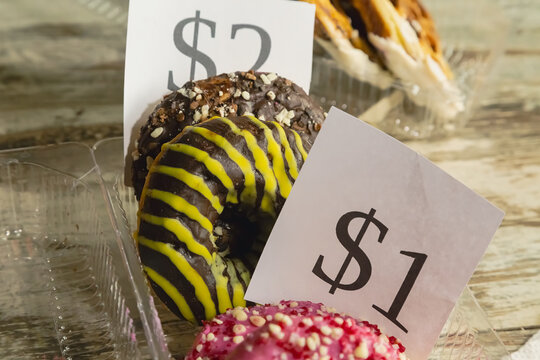 Donuts with chocolate glaze and pink glaze in a clear plastic container with price tags of 1d ollar and $2, close-up, donuts for sale.