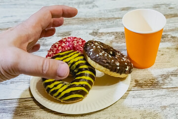 A left hand is about to grab a donut with chocolate cream and glaze from a kitchen table, snack on the go, quick carbohydrates, festive treat.