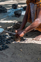 kobieta rozłupująca ręcznie wypalone skorupki orzech&oacute;w nerkowca