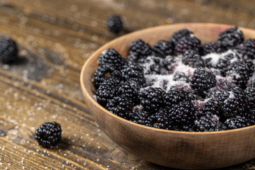 ripe blackberries in a wooden bowl sprinkled with sugar , but ripe blackberries on the table with white sweet sugar, side view
