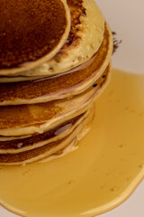 pancakes stacked together on a white bowl, a tower of small milk pancakes on a ceramic bowl with bee honey, close up, side view