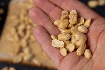 peanut butter on a piece of bread and roasted peanuts on the table, The nuts are in the man's hand