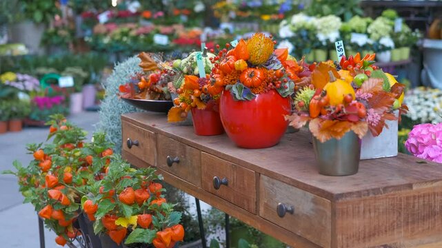 Autumn flowers composition changing on table in flower shop. Colorful autumn flower arrangements featuring pumpkins and berries change positions on a wooden table in a flower shop