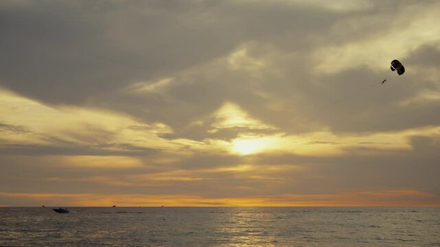 Golden sunset illuminating parasailer soaring over serene ocean, embodying freedom with vibrant thai coastal scenery in breathtaking aerial view