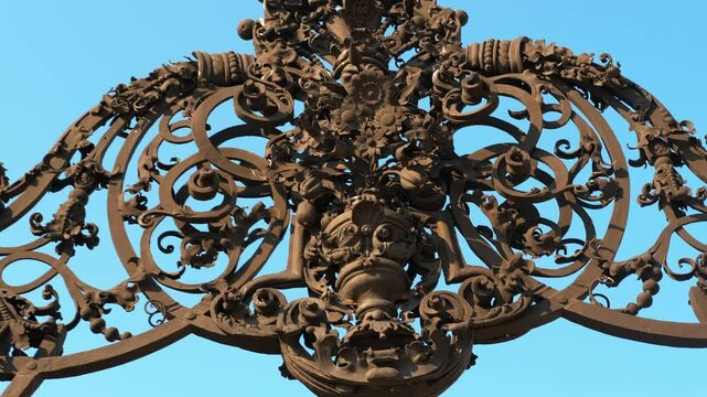 Decorative wrought iron gate detail showcasing intricate floral and foliate patterns, highlighted against a clear blue sky, emphasizing traditional craftsmanship and artistry