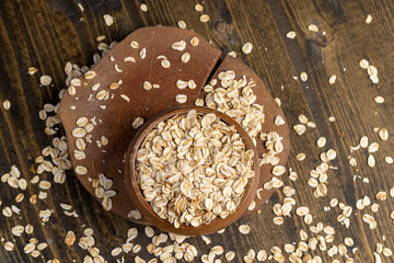 round bowl with oatmeal flakes for making porridge, scattered dry cereal flakes from oats, flattened, steamed and dried, close up, top view