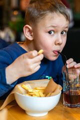 Young boy eating French fries and sipping a drink through a straw at a restaurant table close-up...