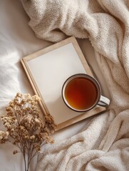 Cozy scene featuring a cup of tea on a wooden tray with a blank notepad and dried flowers
