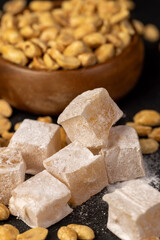 Turkish delight with peanut kernels scattered on a black slate board, oriental sweets made from sugar and molasses with peanuts , closeup