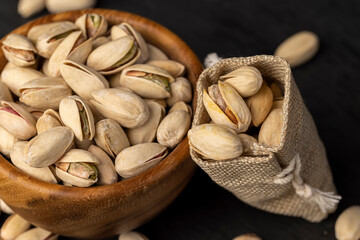 unpeeled pistachio nuts with cracked shells, poured into a wooden bowl and a coarse bag, close up,...