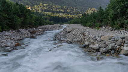 The bubbling clear water of a mountain river flows over large rocks high in the mountains. Ecologically clean water flows down from a glacier in the mountains. Nature in the mountains.
