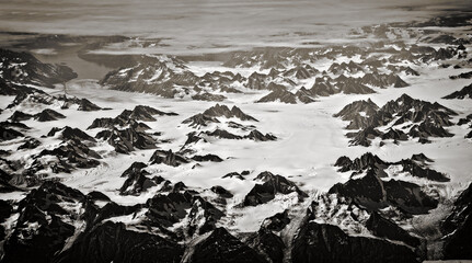 Greenland landscape aerial view, the mountains are covered in snow. Western coast of Greenland. Plane view of mountain peaks. Black and white image of a snowy mountain range