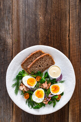 Salmon appetizer - cold smoked salmon, hard boiled eggs, leafy greens and mayonnaise with bread on wooden table	