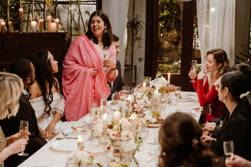 The wedding guests toast the bride and groom during an elegant indoor reception dinner. Adults smile and raise champagne glasses around a beautifully decorated table with candles and flowers.