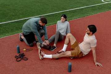 Sports injury during training, physiotherapist providing first aid to athlete on running track