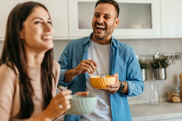 Happy couple laughing and eating breakfast in kitchen