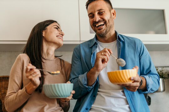 Happy couple enjoying breakfast and laughing together in kitchen