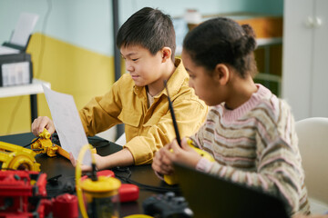 Young boy and girl working on science project together at school, focusing on instructions and...
