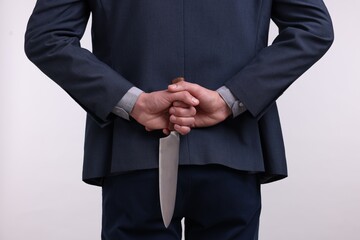 Businessman holding knife behind his back on white background, closeup
