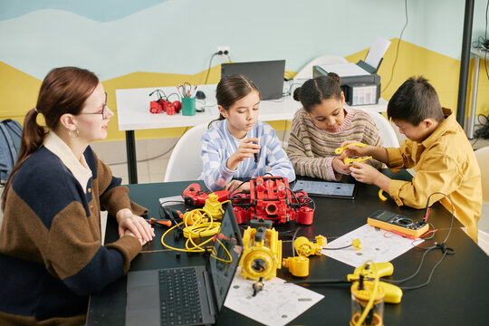 Group of children actively engaging in STEM activities with various tools and devices under supervision of educator in classroom setting