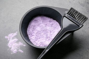 Bowl with hair bleaching powder and brush on grey table, closeup
