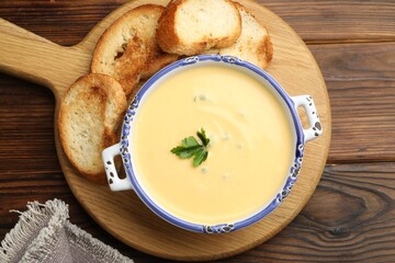 Tasty cheese dipping sauce in bowl and croutons on wooden table, top view