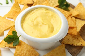 Tasty dipping cheese sauce in bowl and nacho chips on table, closeup