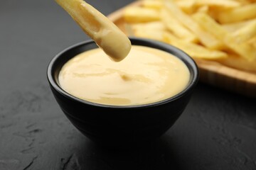Dipping French fry into cheese sauce at black table, closeup