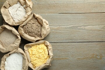 Different types of flour in paper bags on wooden table, flat lay. Space for text