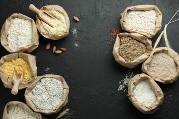 Different types of flour in paper bags on black table, flat lay. Space for text