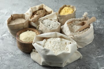 Different types of flour in bags on grey textured table, closeup