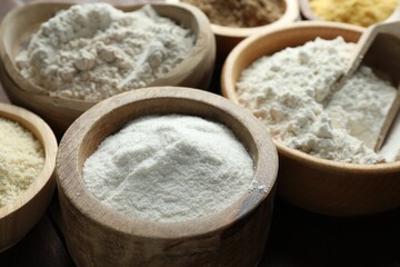 Different types of flour in bowls on wooden table, closeup