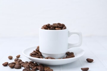 Aromatic coffee beans, cup and saucer on white table, closeup