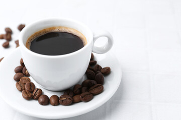 Aromatic coffee in cup and beans on white table, closeup. Space for text
