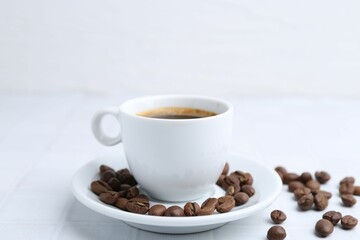 Aromatic coffee in cup and beans on white table, closeup