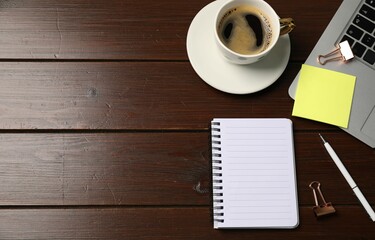 Notebook, sticky note, pen, binder clips, coffee and laptop on wooden table, flat lay. Space for text