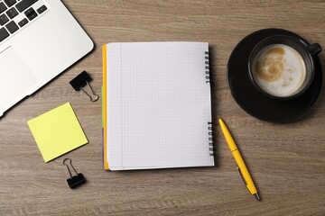 Notebook, sticky note, pen, binder clips, coffee and laptop on wooden table, flat lay