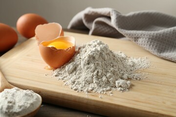 Pile of flour and broken egg on wooden table against grey background, closeup