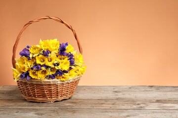 Wicker basket with beautiful flowers on wooden table against coral background. Space for text