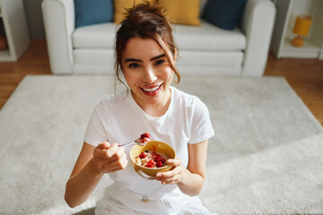 Young woman enjoying a healthy breakfast of oatmeal with berries in her living room
