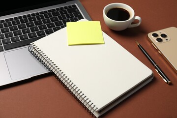 Notebook with pen, laptop, smartphone, sticky note and coffee on brown background, closeup